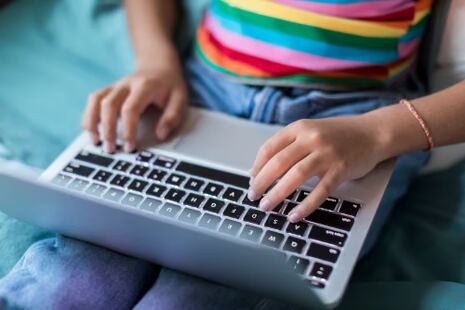 A child's hands typing on a laptop at home