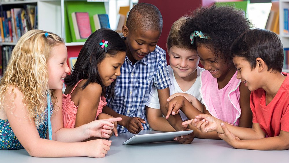 Six elementary school students gathered around a tablet in their school library